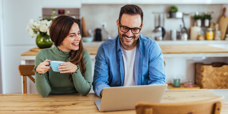 happy couple sitting at kitchen table researching credit tips on their laptop