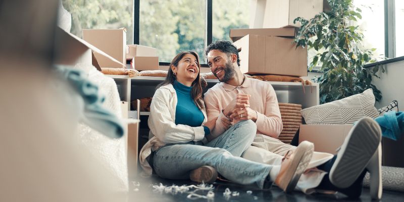 Happy husband and wife sitting on floor of new home surrounded by moving boxes